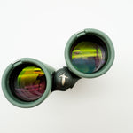 A pair of green binoculars displayed upright on a white branded stand against a clean white background.