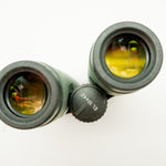A pair of green binoculars displayed upright on a white branded stand against a clean white background.