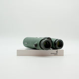A pair of green binoculars displayed upright on a white branded stand against a clean white background.