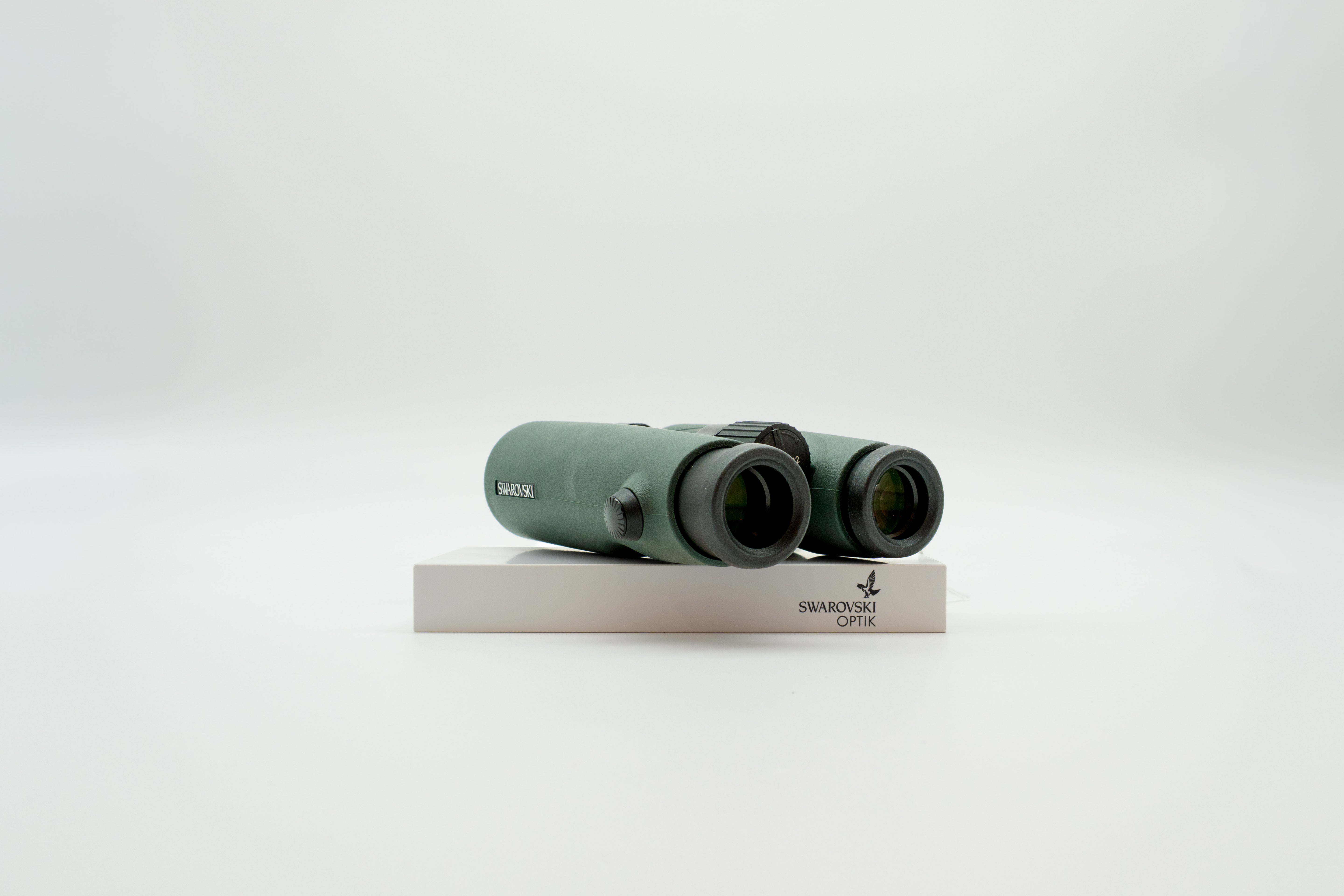 A pair of green binoculars displayed upright on a white branded stand against a clean white background.