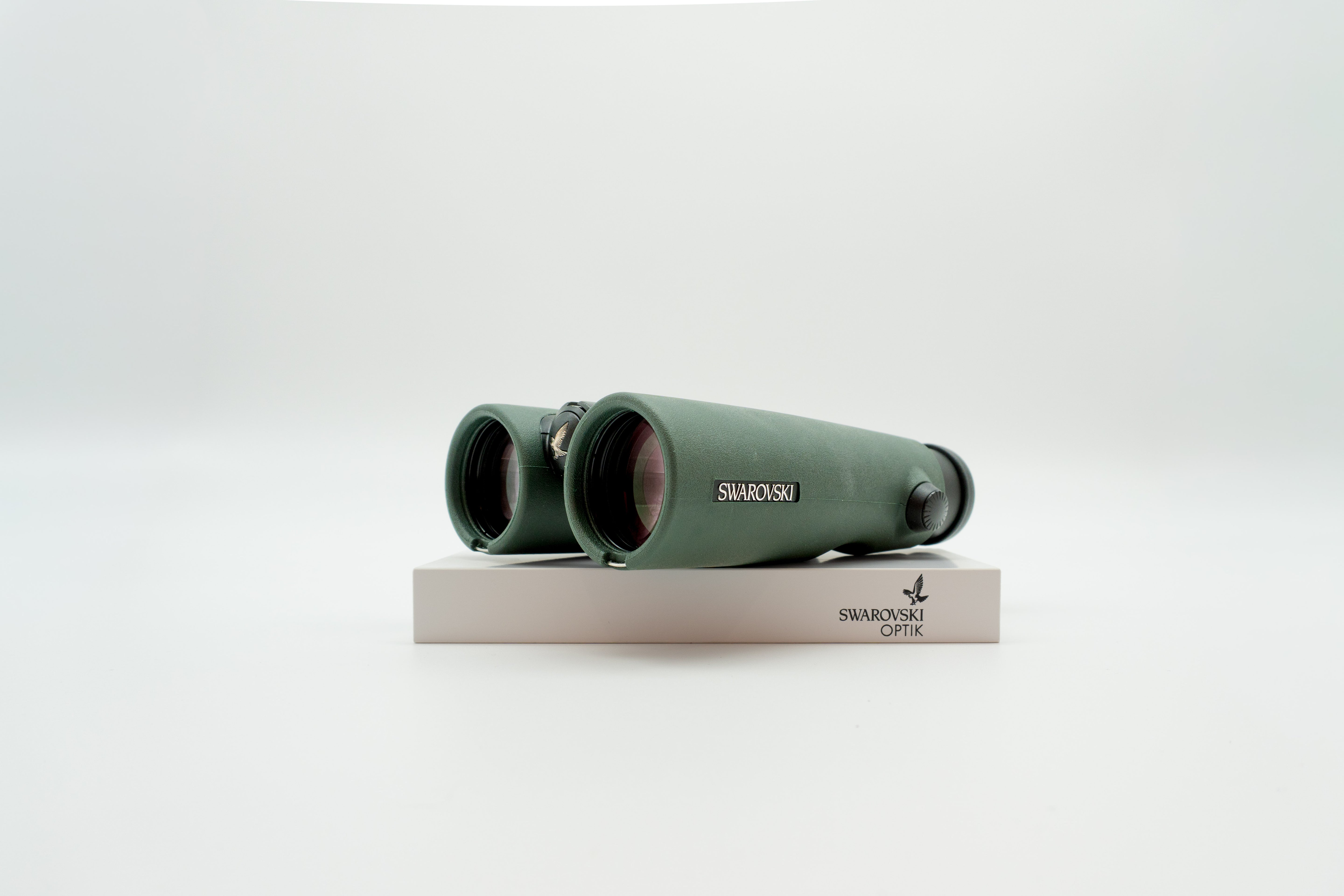 A pair of green binoculars displayed upright on a white branded stand against a clean white background.