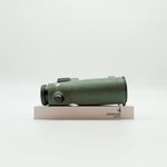 A pair of green SWAROVSKI binoculars standing upright on a small white display block.