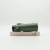 A pair of green SWAROVSKI binoculars standing upright on a small white display block.