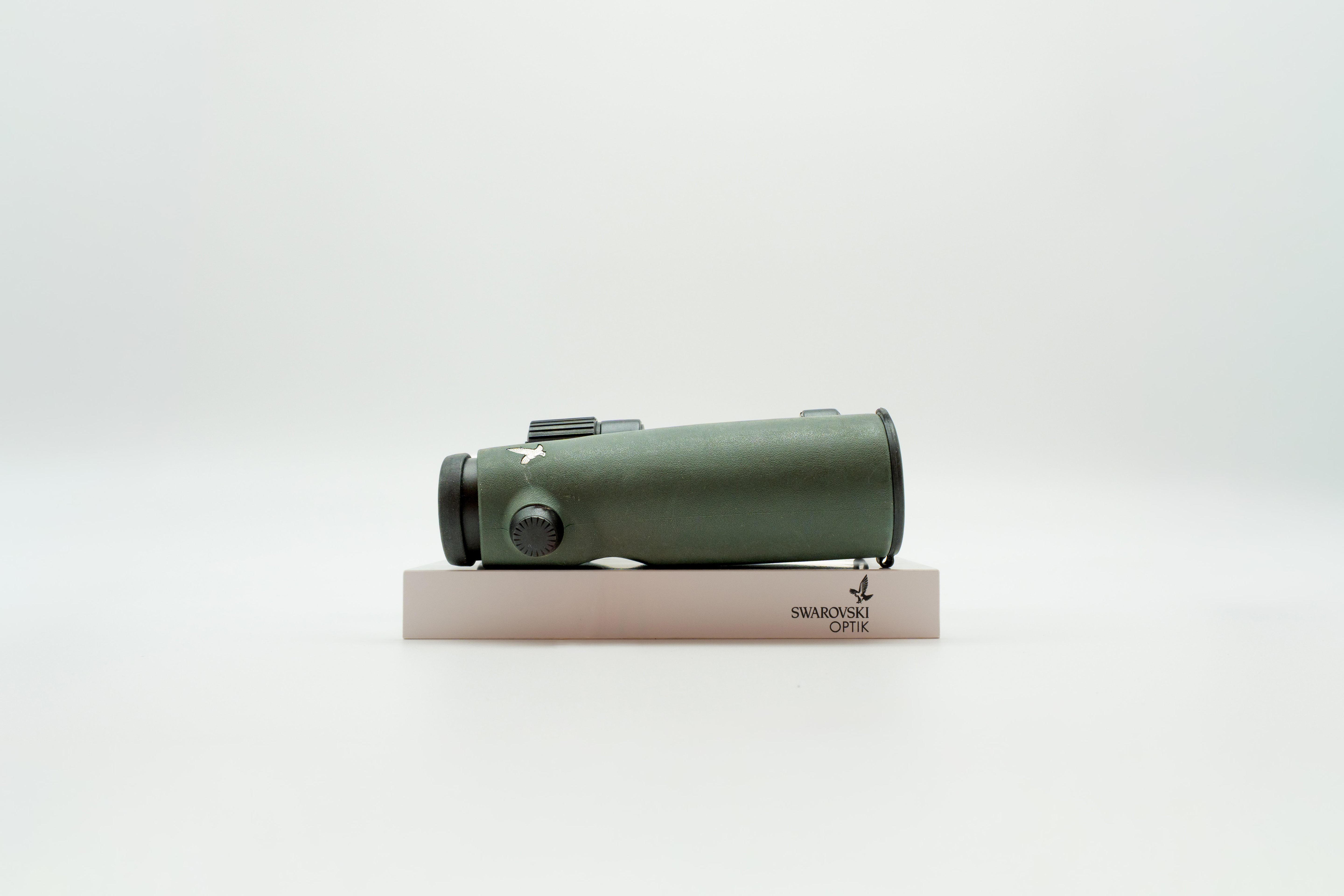 A pair of green SWAROVSKI binoculars standing upright on a small white display block.