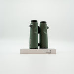 A pair of green SWAROVSKI binoculars standing upright on a small white display block.