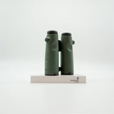 A pair of green SWAROVSKI binoculars standing upright on a small white display block.