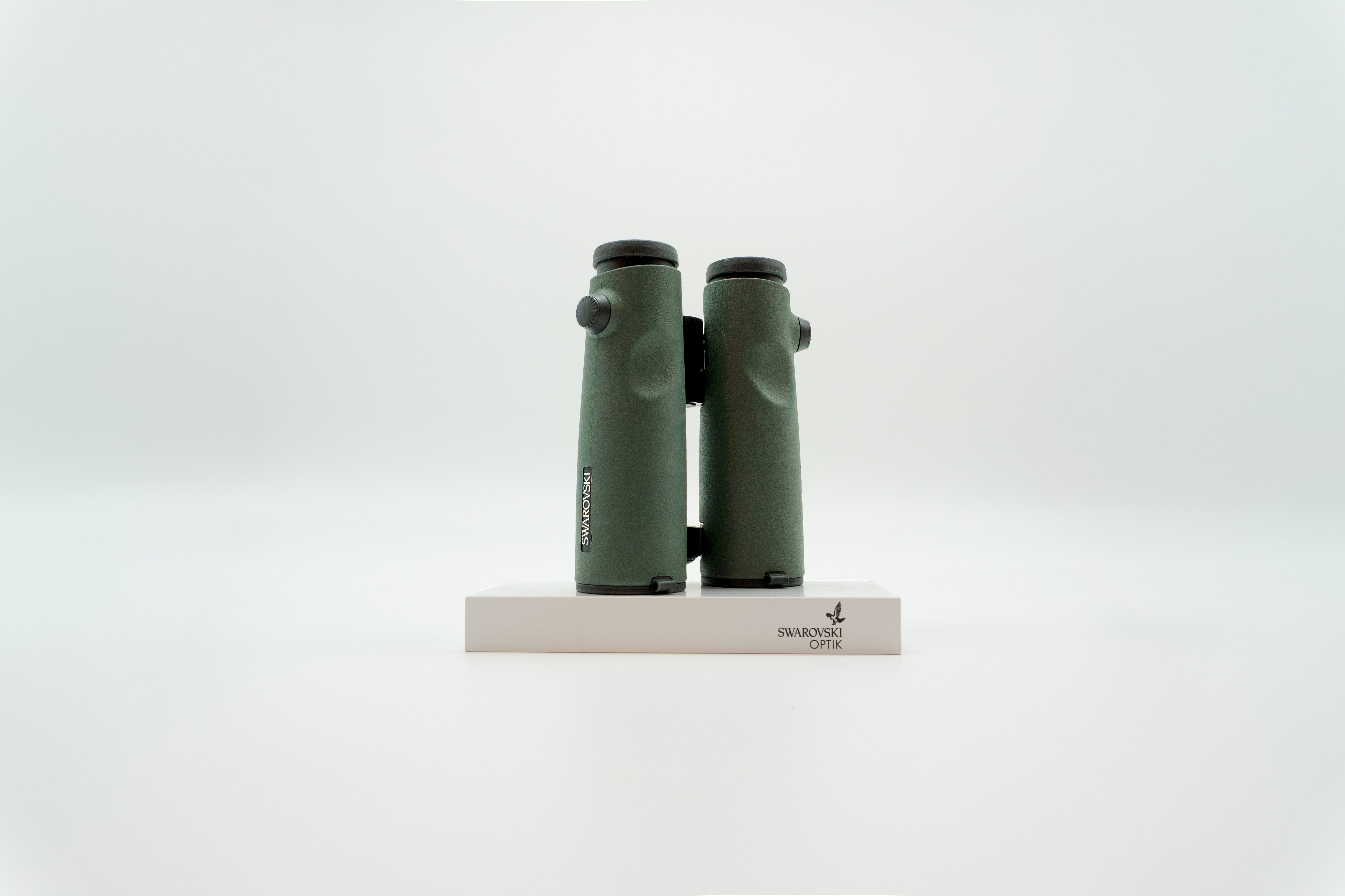 A pair of green SWAROVSKI binoculars standing upright on a small white display block.