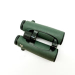 A pair of green SWAROVSKI binoculars standing upright on a small white display block.
