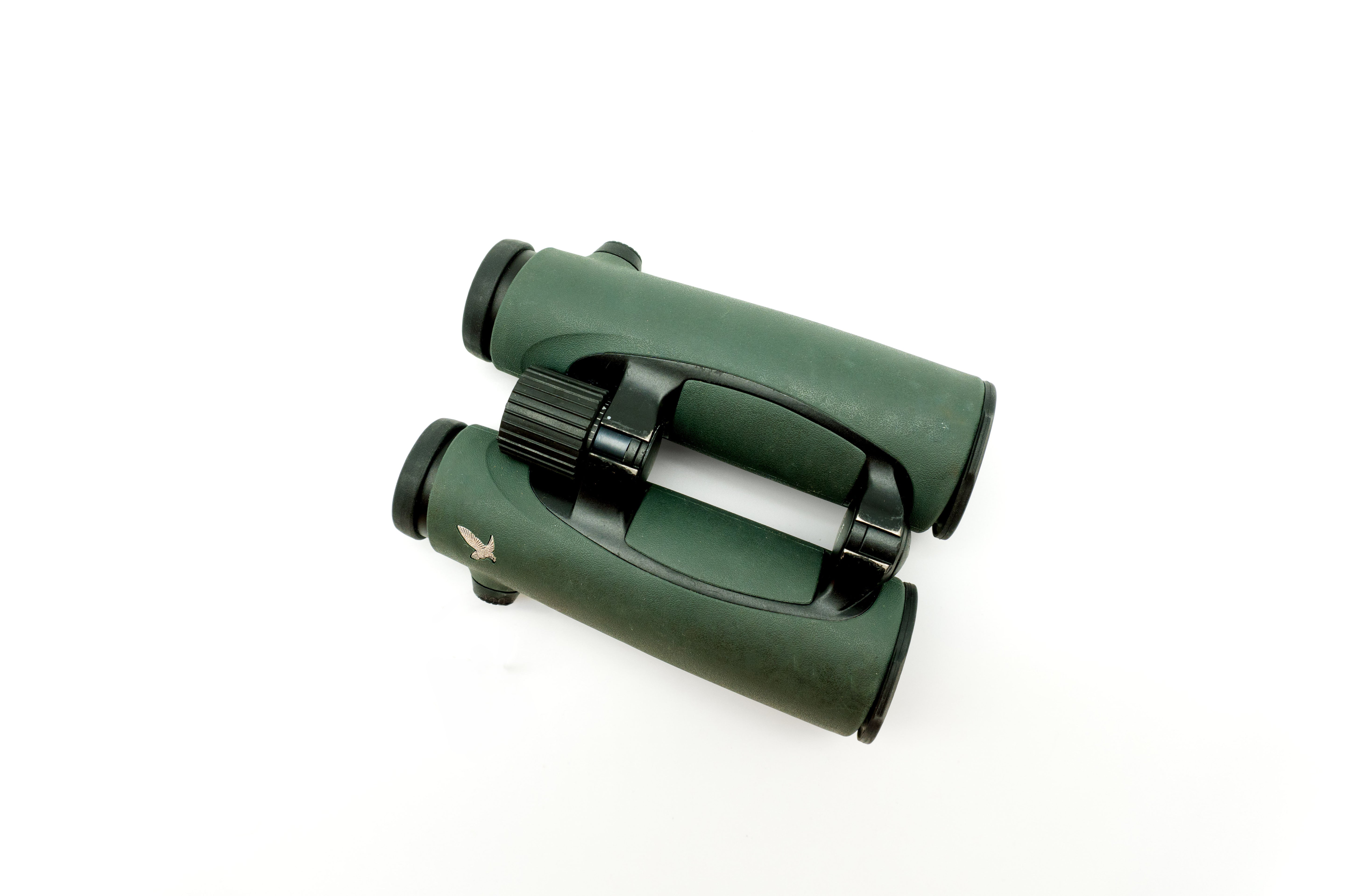 A pair of green SWAROVSKI binoculars standing upright on a small white display block.