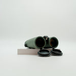 A pair of green SWAROVSKI binoculars standing upright on a small white display block.