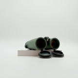 A pair of green SWAROVSKI binoculars standing upright on a small white display block.