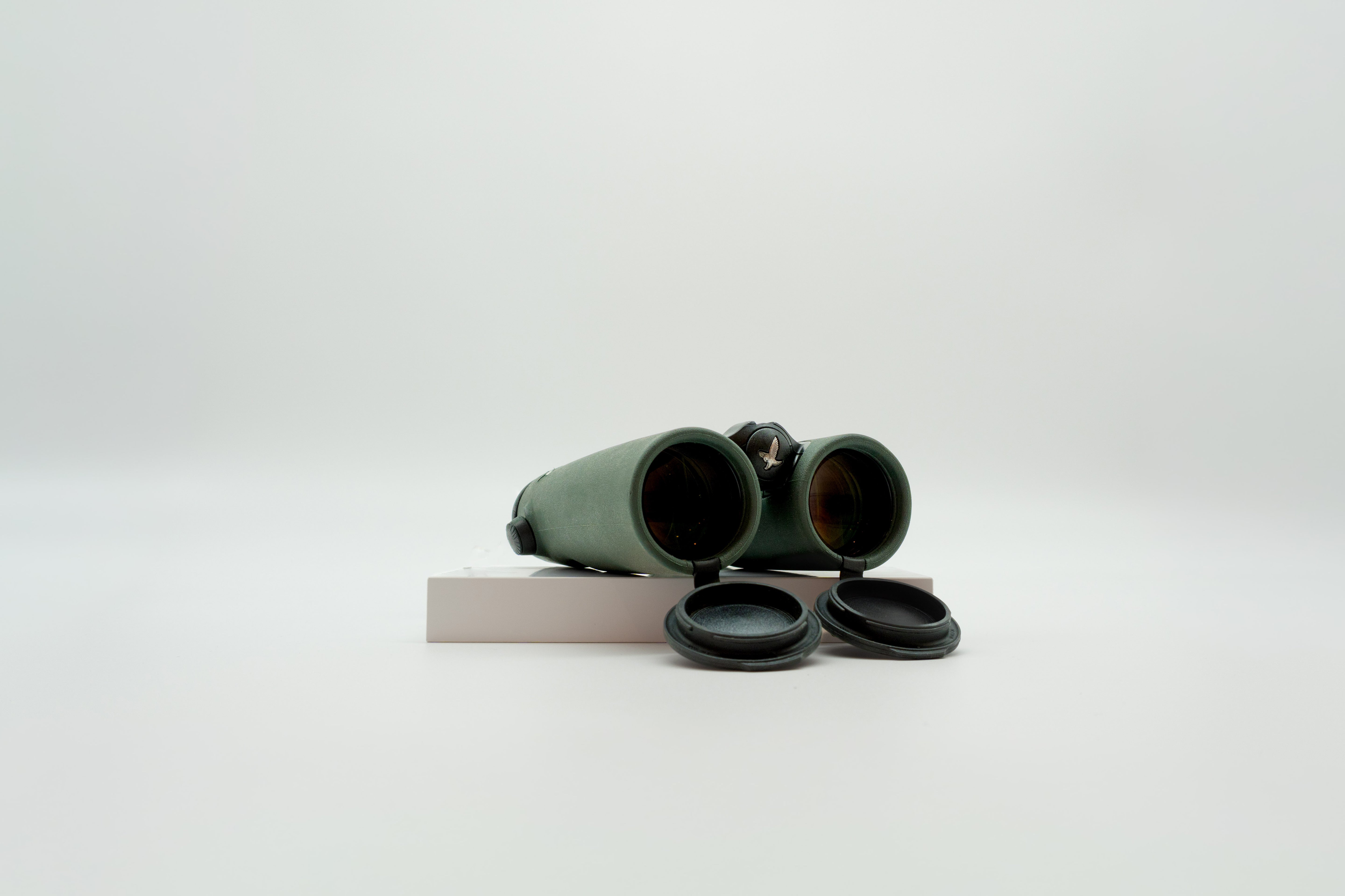 A pair of green SWAROVSKI binoculars standing upright on a small white display block.