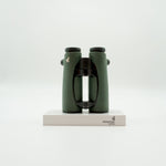 A pair of green SWAROVSKI binoculars standing upright on a small white display block.