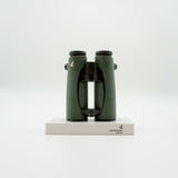 A pair of green SWAROVSKI binoculars standing upright on a small white display block.