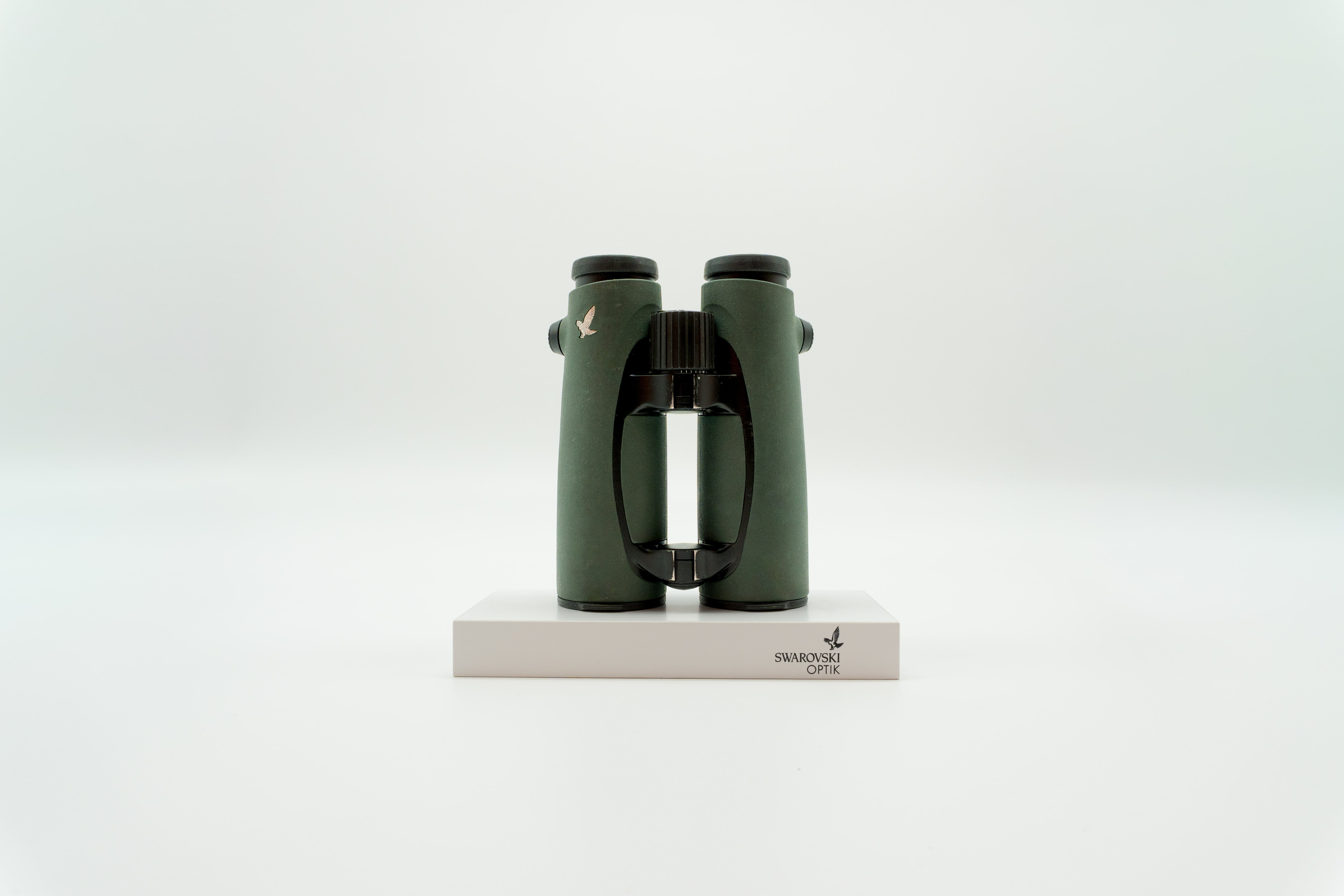 A pair of green SWAROVSKI binoculars standing upright on a small white display block.