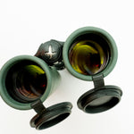 A pair of green SWAROVSKI binoculars standing upright on a small white display block.