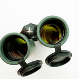 A pair of green SWAROVSKI binoculars standing upright on a small white display block.