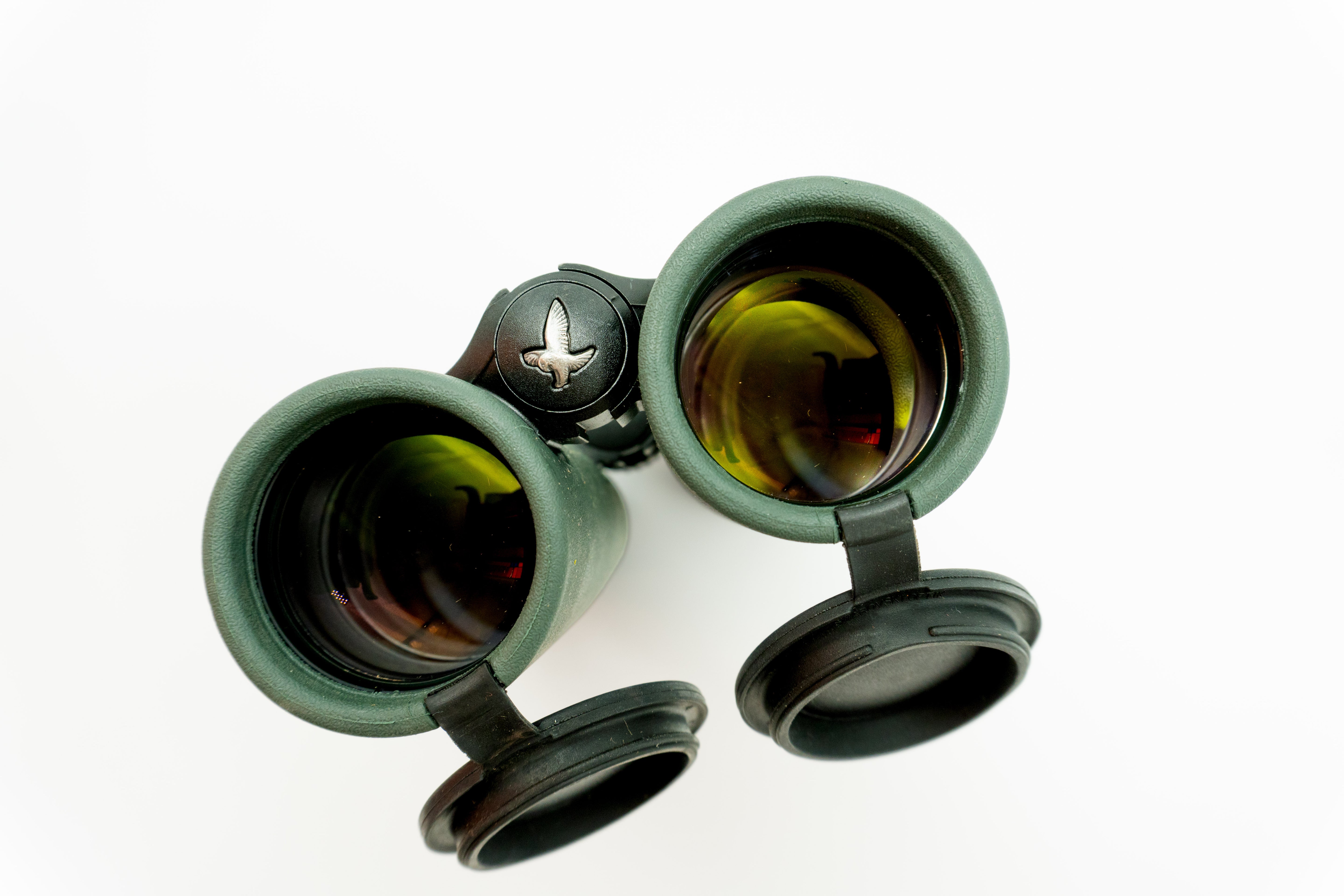 A pair of green SWAROVSKI binoculars standing upright on a small white display block.