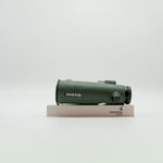 A pair of green SWAROVSKI binoculars standing upright on a small white display block.