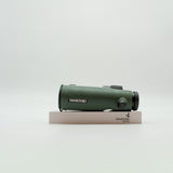 A pair of green SWAROVSKI binoculars standing upright on a small white display block.
