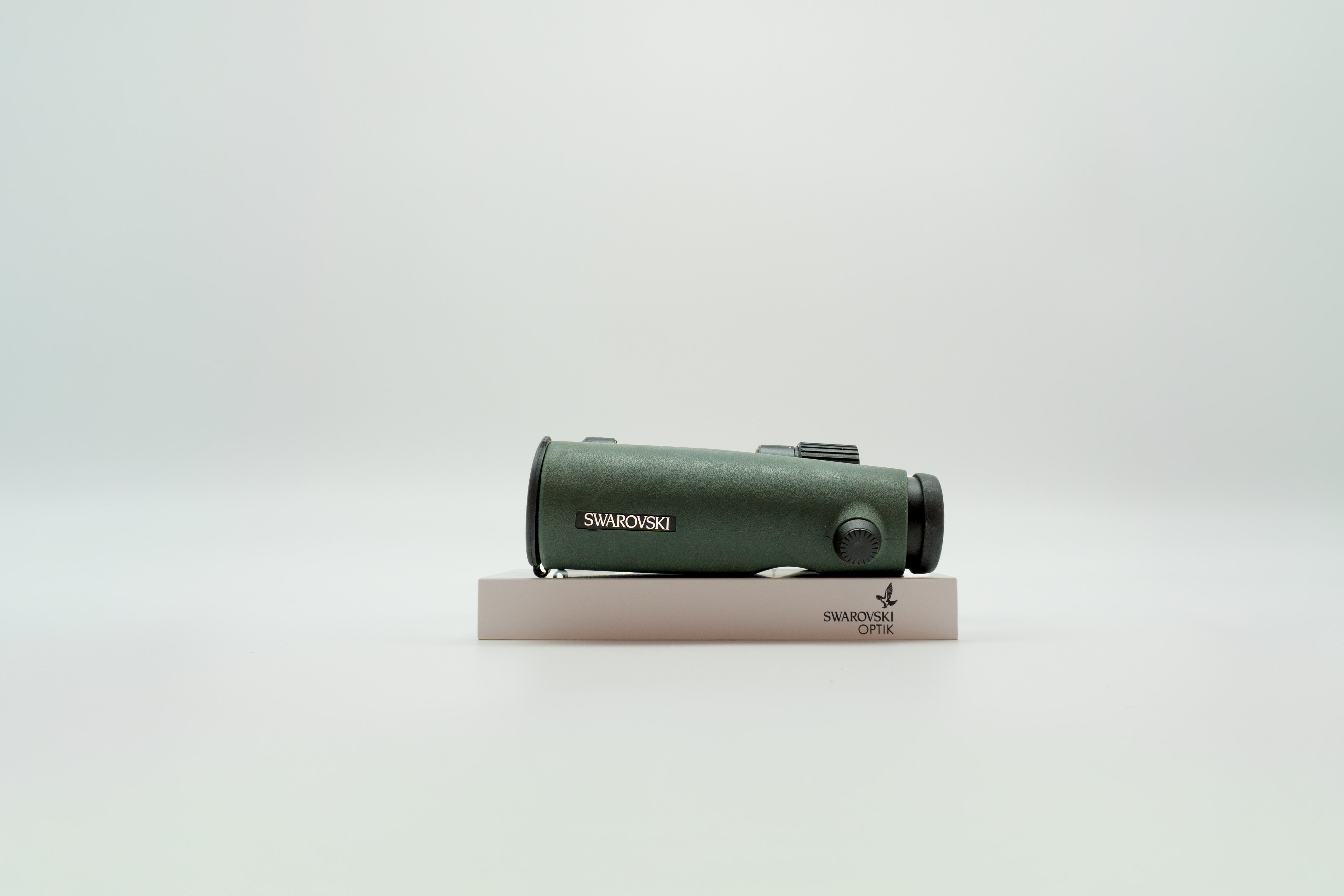 A pair of green SWAROVSKI binoculars standing upright on a small white display block.