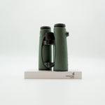 A pair of green SWAROVSKI binoculars standing upright on a small white display block.