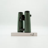 A pair of green SWAROVSKI binoculars standing upright on a small white display block.