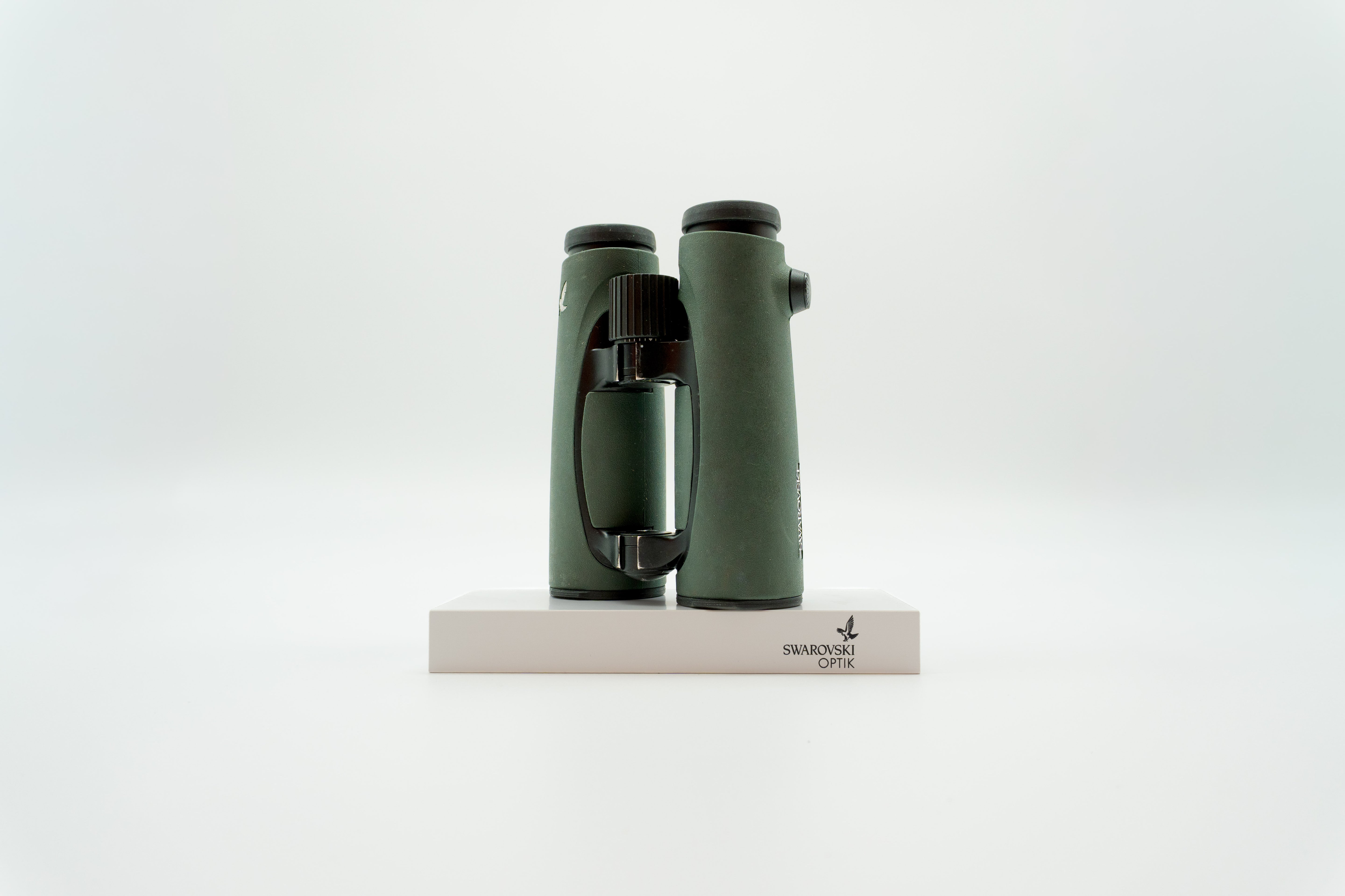 A pair of green SWAROVSKI binoculars standing upright on a small white display block.