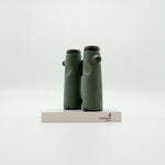 A pair of green SWAROVSKI binoculars standing upright on a small white display block.