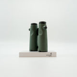 A pair of green SWAROVSKI binoculars standing upright on a small white display block.