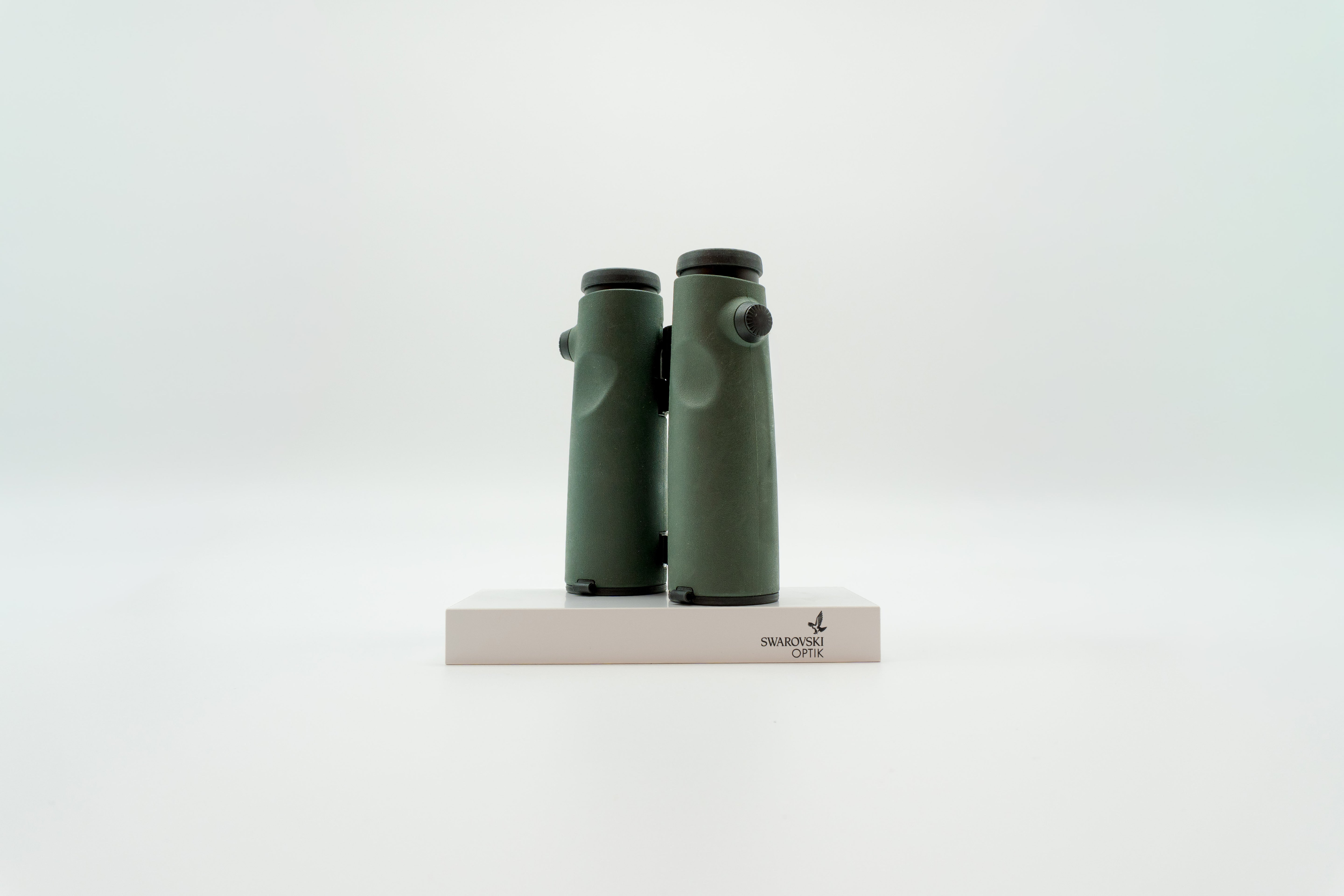 A pair of green SWAROVSKI binoculars standing upright on a small white display block.