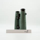 A pair of green binoculars displayed upright on a white branded stand against a clean white background.