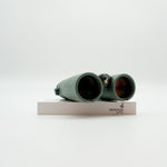 A pair of green binoculars displayed upright on a white branded stand against a clean white background.