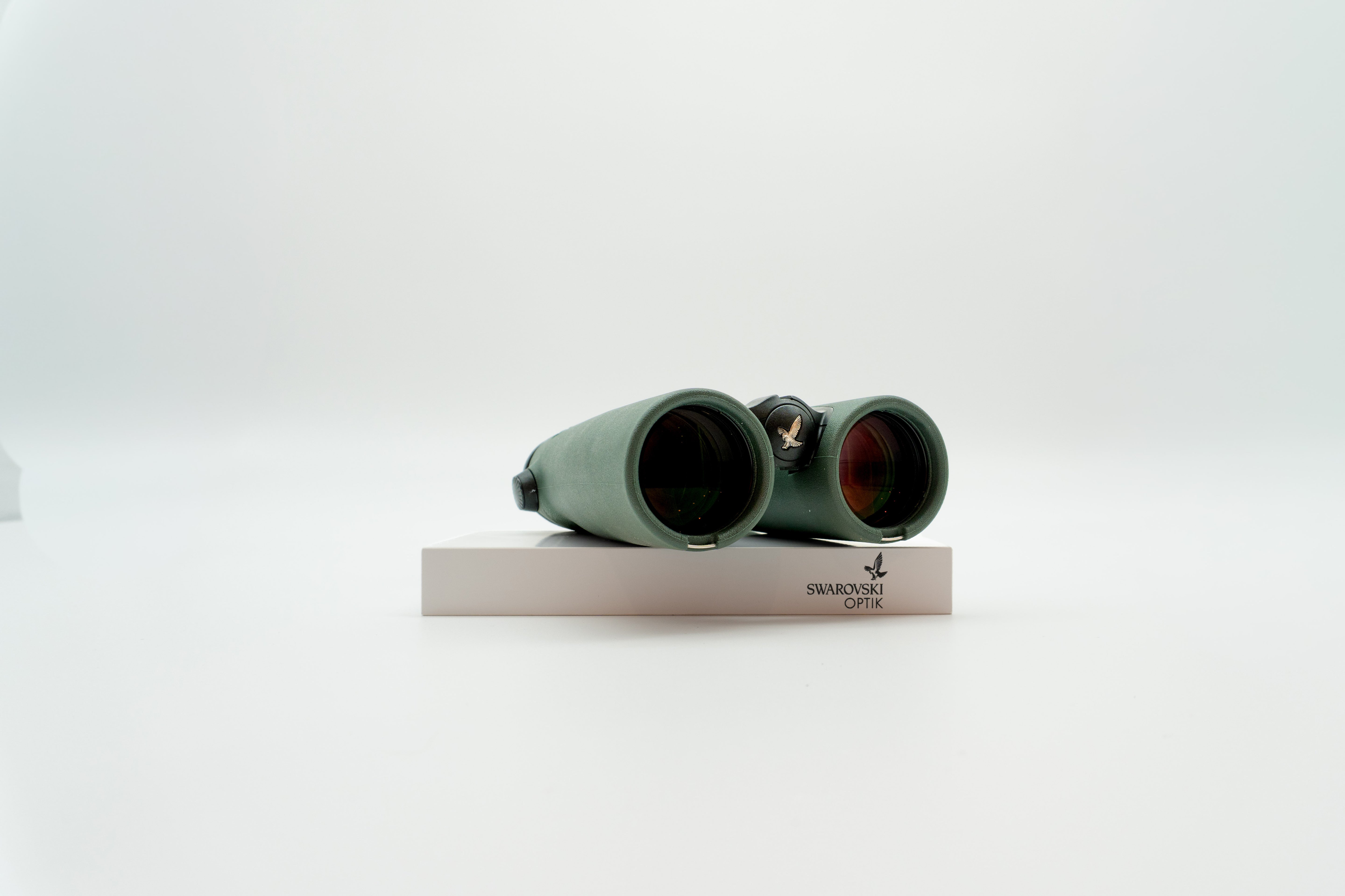 A pair of green binoculars displayed upright on a white branded stand against a clean white background.
