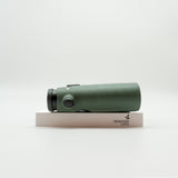 A pair of green binoculars displayed upright on a white branded stand against a clean white background.