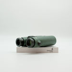 A pair of green binoculars displayed upright on a white branded stand against a clean white background.