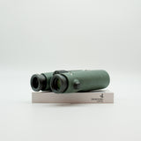 A pair of green binoculars displayed upright on a white branded stand against a clean white background.