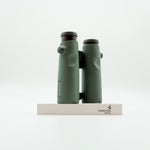A pair of green binoculars displayed upright on a white branded stand against a clean white background.