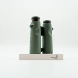 A pair of green binoculars displayed upright on a white branded stand against a clean white background.