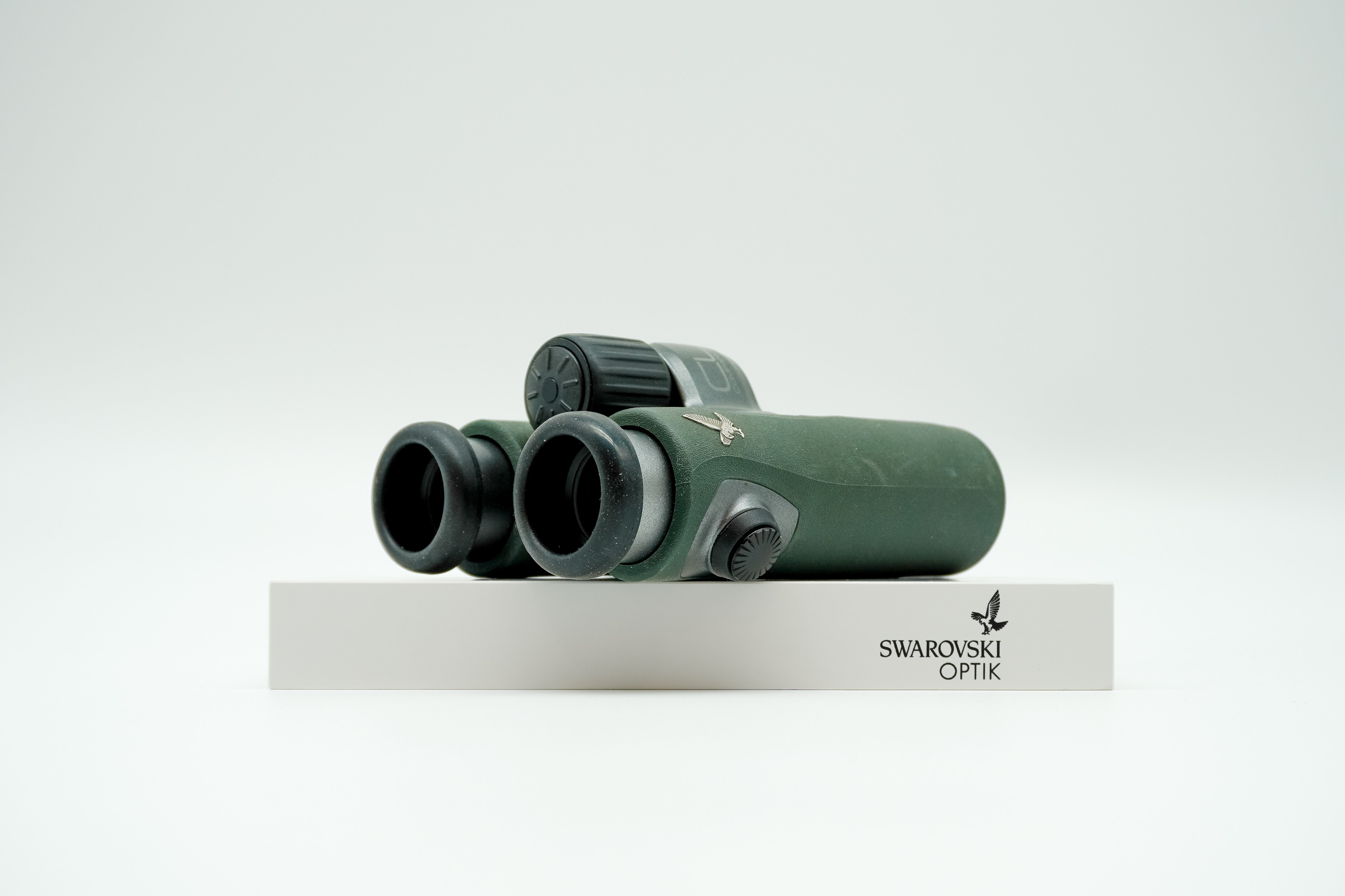 SWAROVSKI green cl pocket binoculars with white background on a stand.