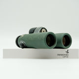 SWAROVSKI green cl pocket binoculars with white background on a stand.