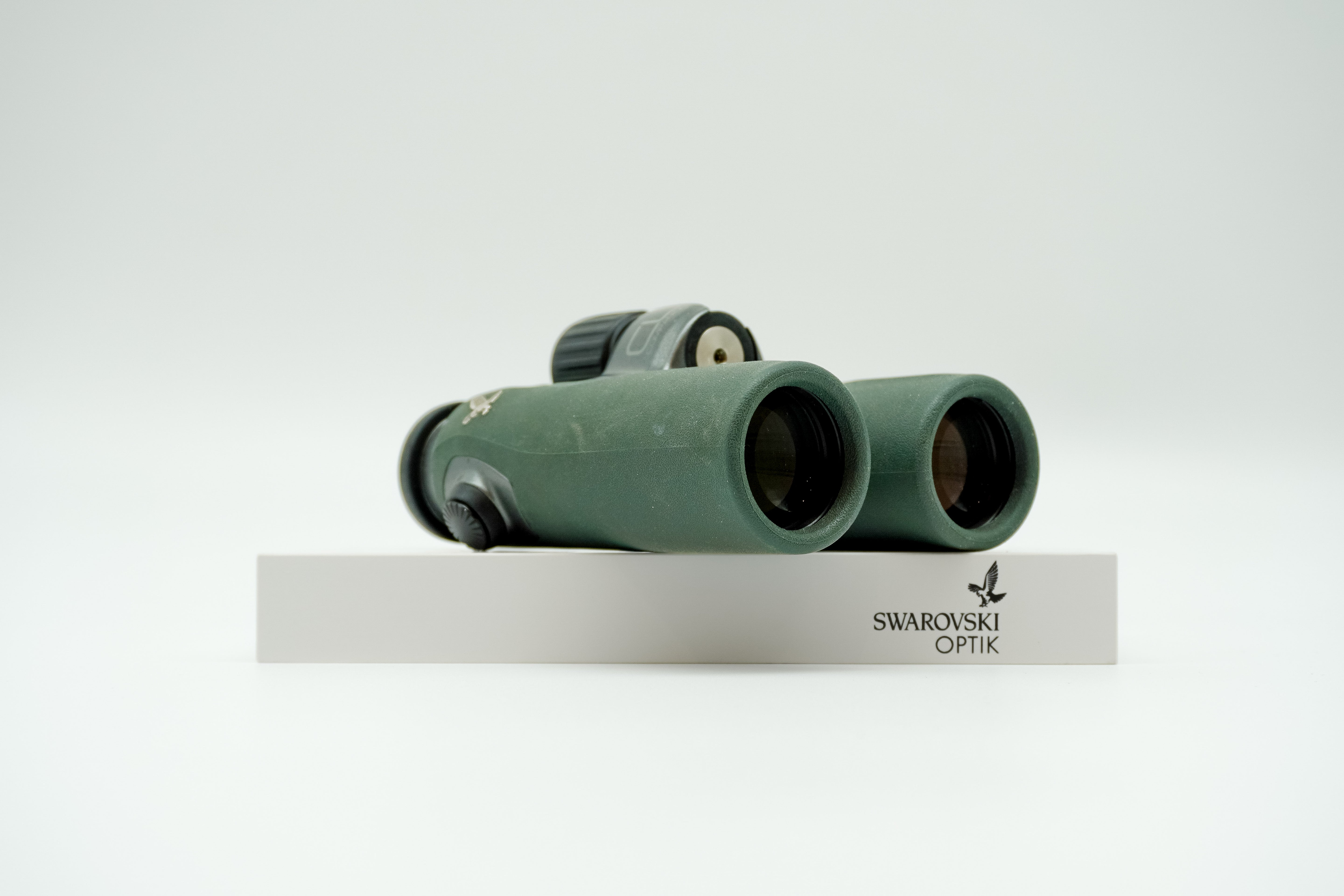 SWAROVSKI green cl pocket binoculars with white background on a stand.