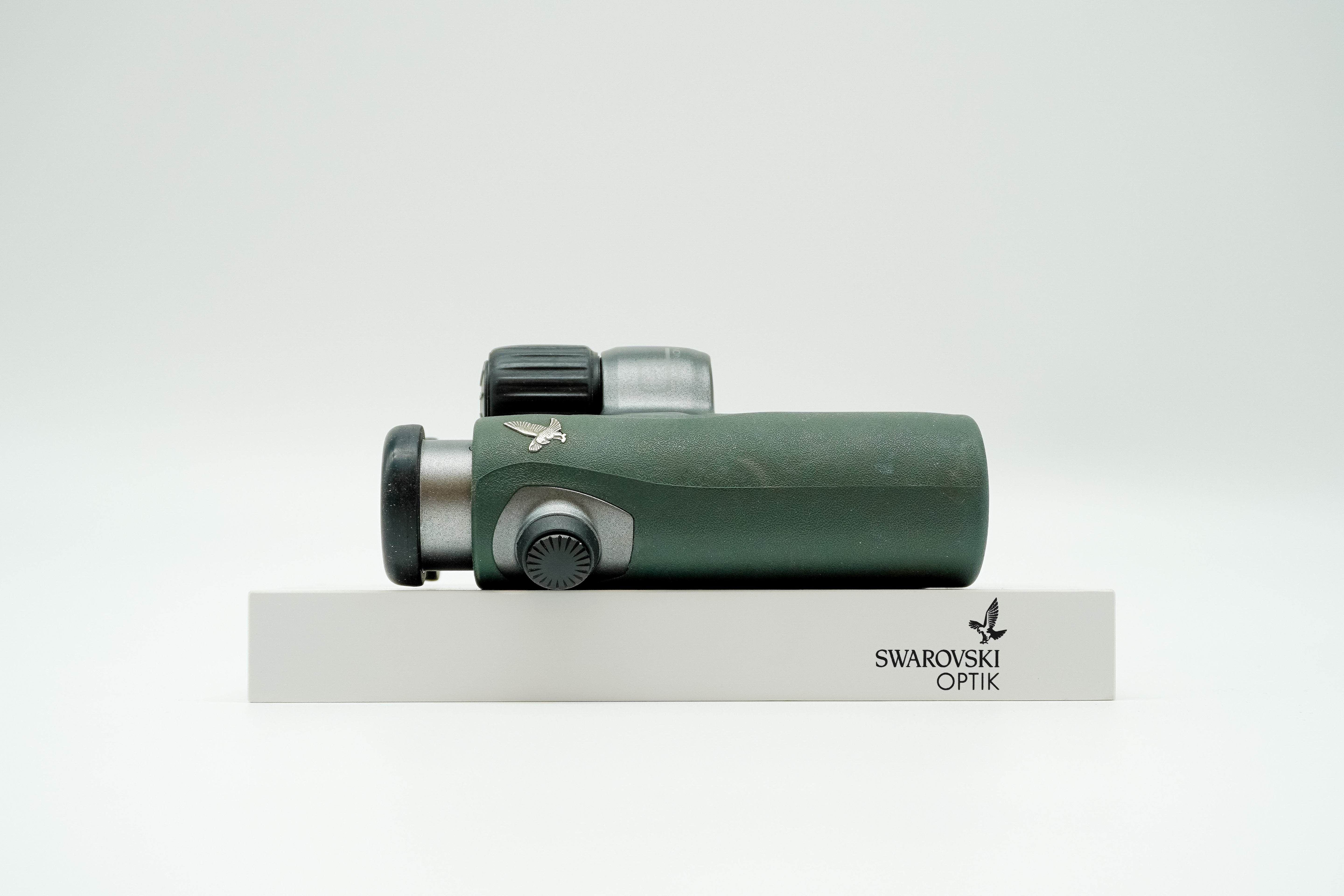 SWAROVSKI green cl pocket binoculars with white background on a stand.