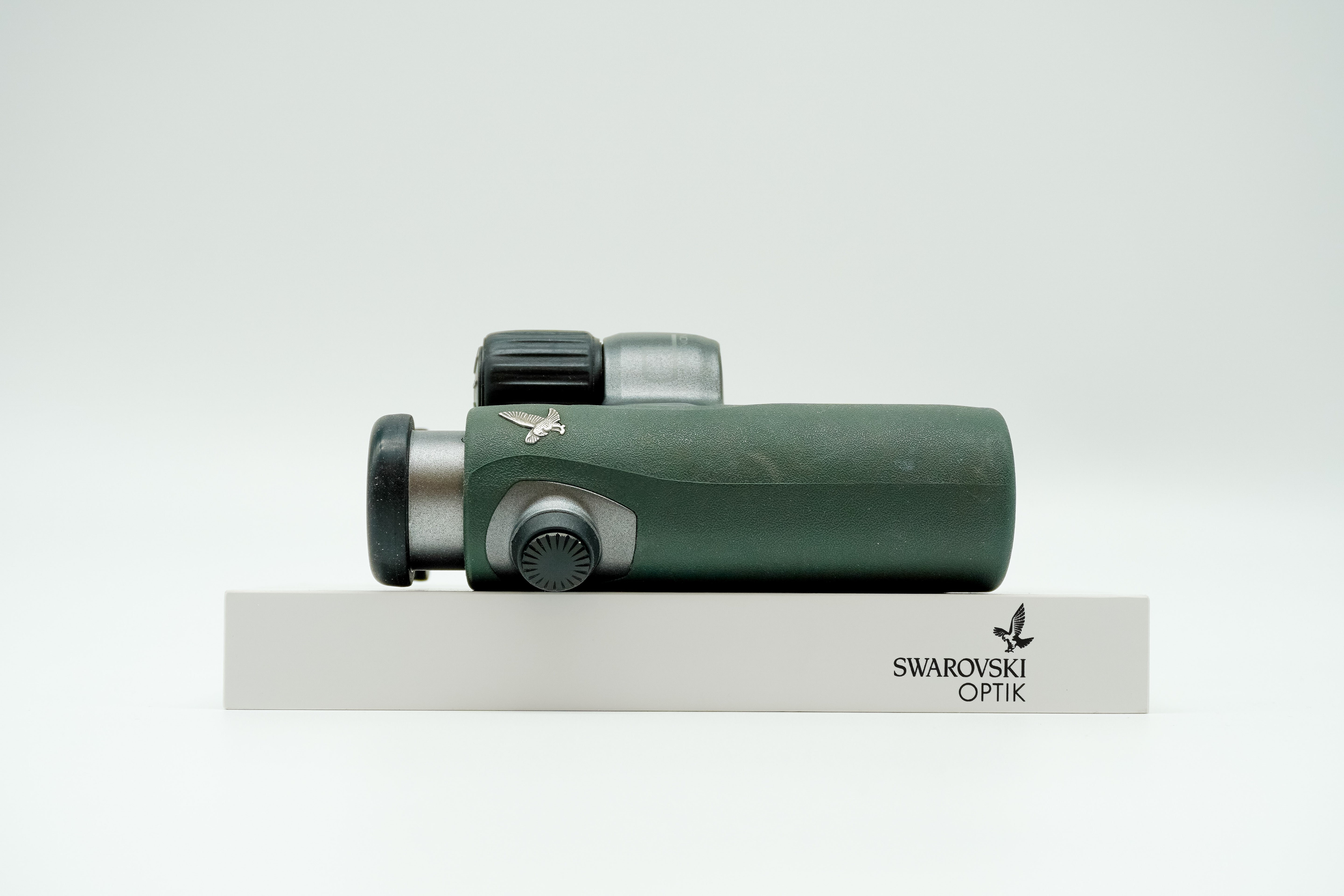SWAROVSKI green cl pocket binoculars with white background on a stand.