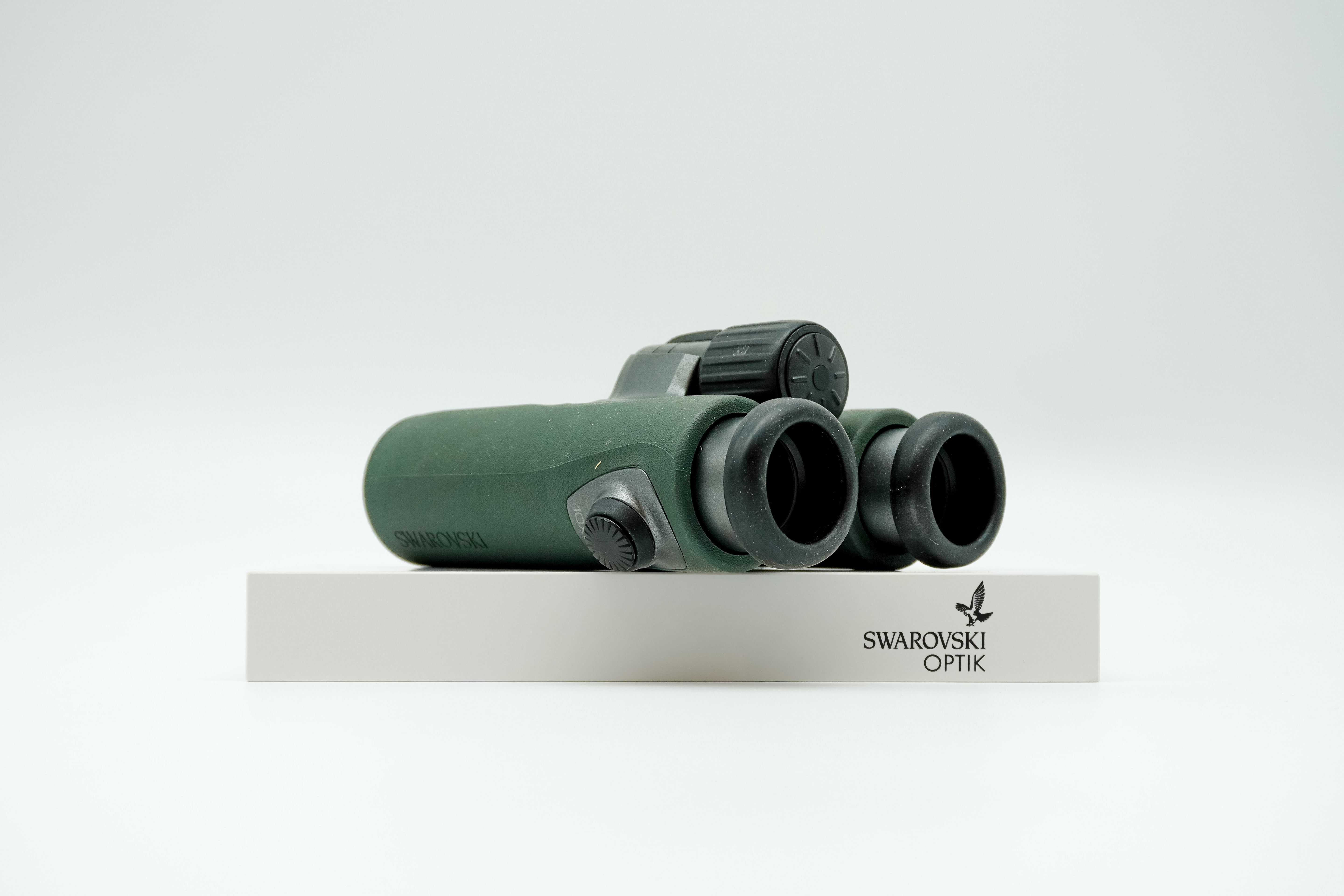 SWAROVSKI green cl pocket binoculars with white background on a stand.