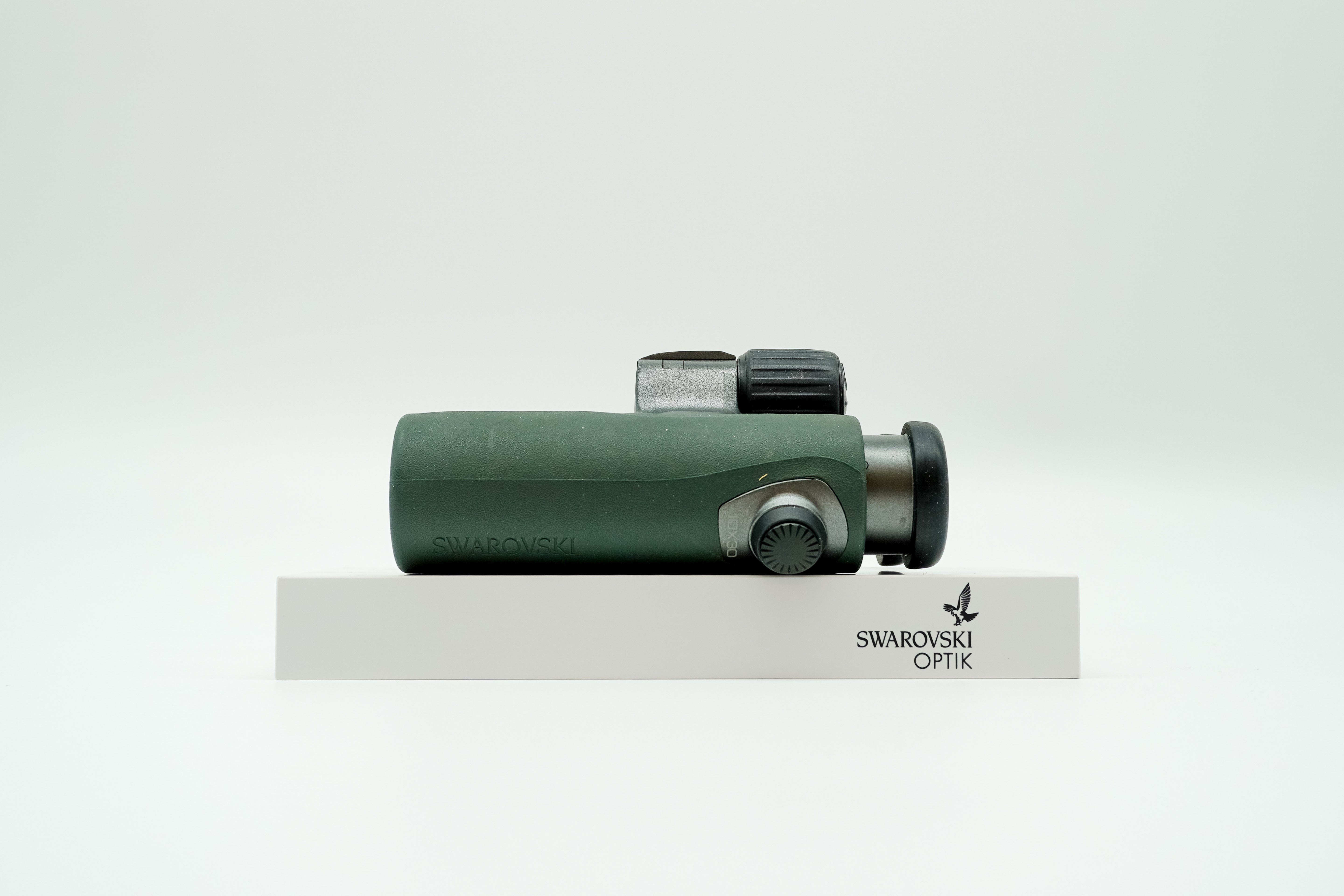 SWAROVSKI green cl pocket binoculars with white background on a stand.