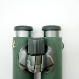 SWAROVSKI green cl pocket binoculars with white background on a stand.